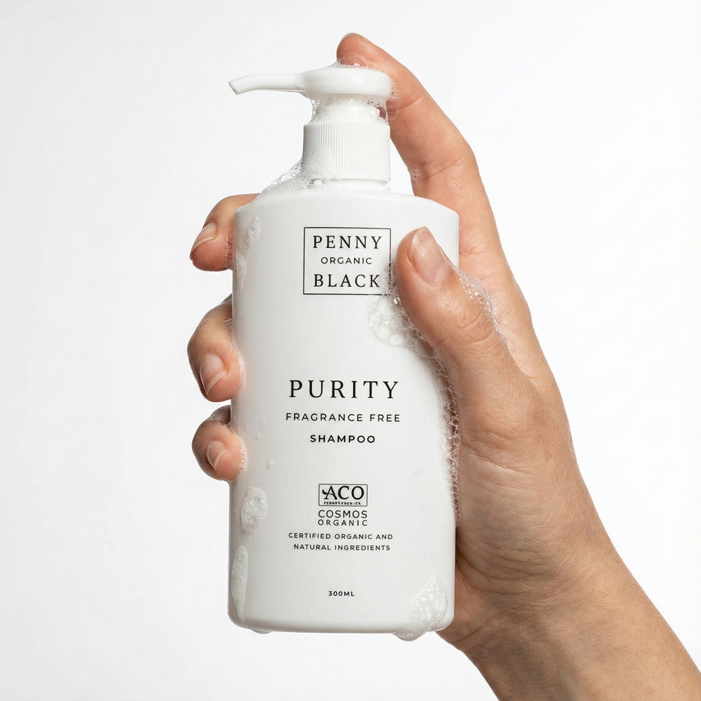 Hand holding a bottle of Penny Organic Black Purity Fragrance Free Shampoo on a white background