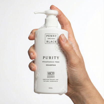 Hand holding a bottle of Penny Organic Black Purity Fragrance Free Shampoo on a white background